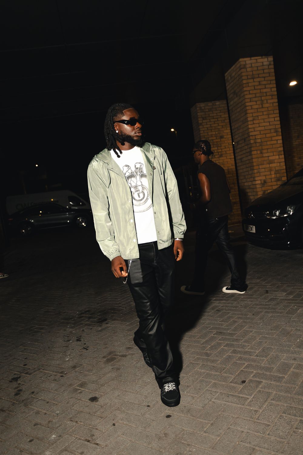 A person walking at night wearing a light-colored jacket and dark pants on a brick-paved path.