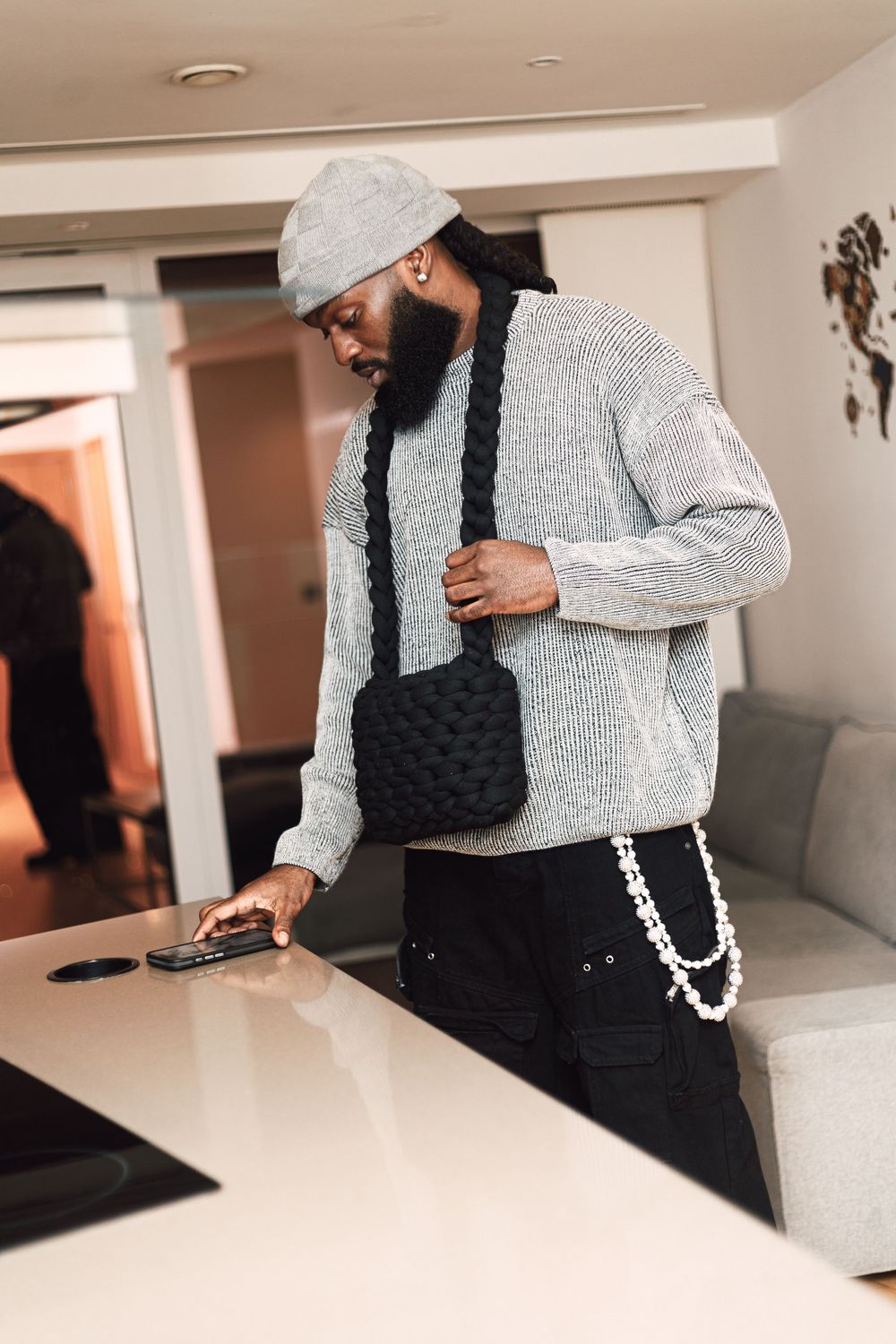 Person wearing a gray sweater and black overalls uses a mobile device while sitting on a white couch.