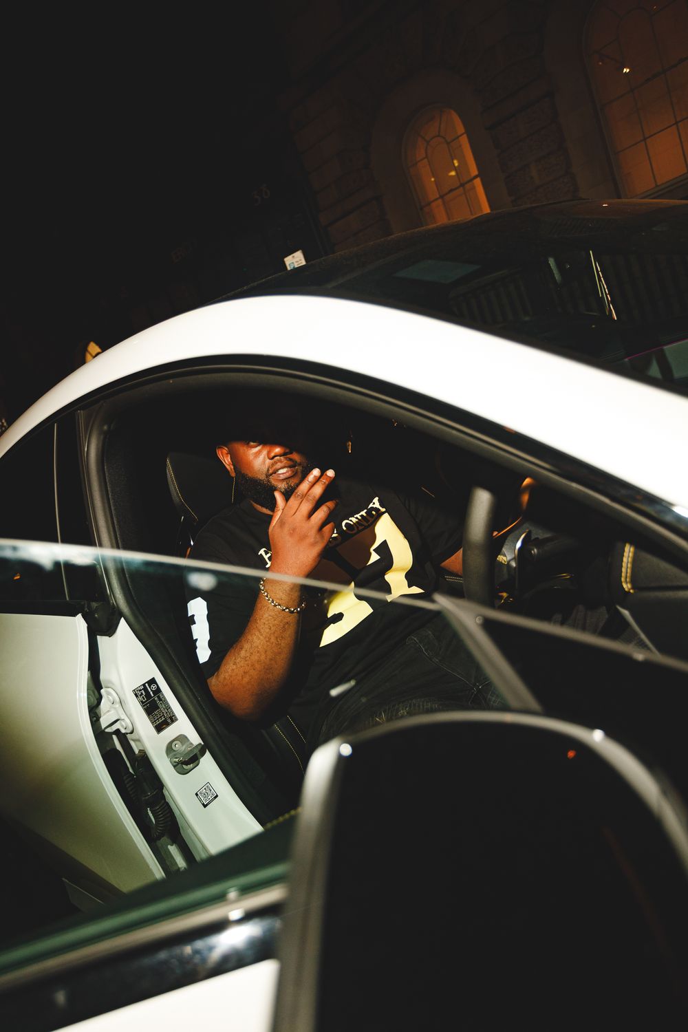 Person making a hand gesture while sitting in the driver's seat of a white car at night.