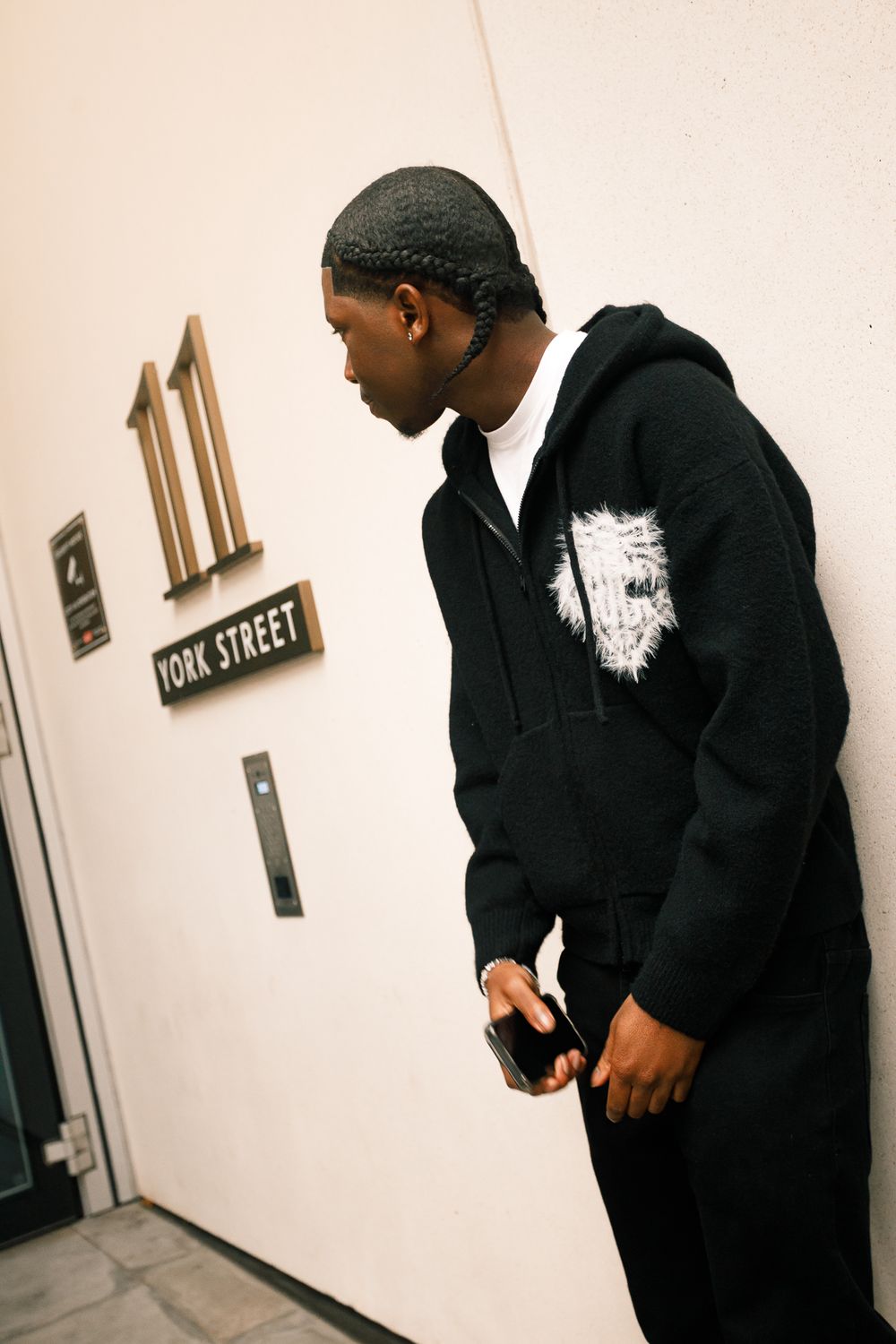 Two people in dark hoodies standing in white hallway near wall sign.