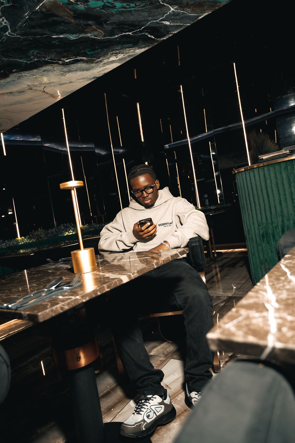 A person in a white hoodie sits in a dimly lit space with vertical light fixtures casting dramatic shadows.