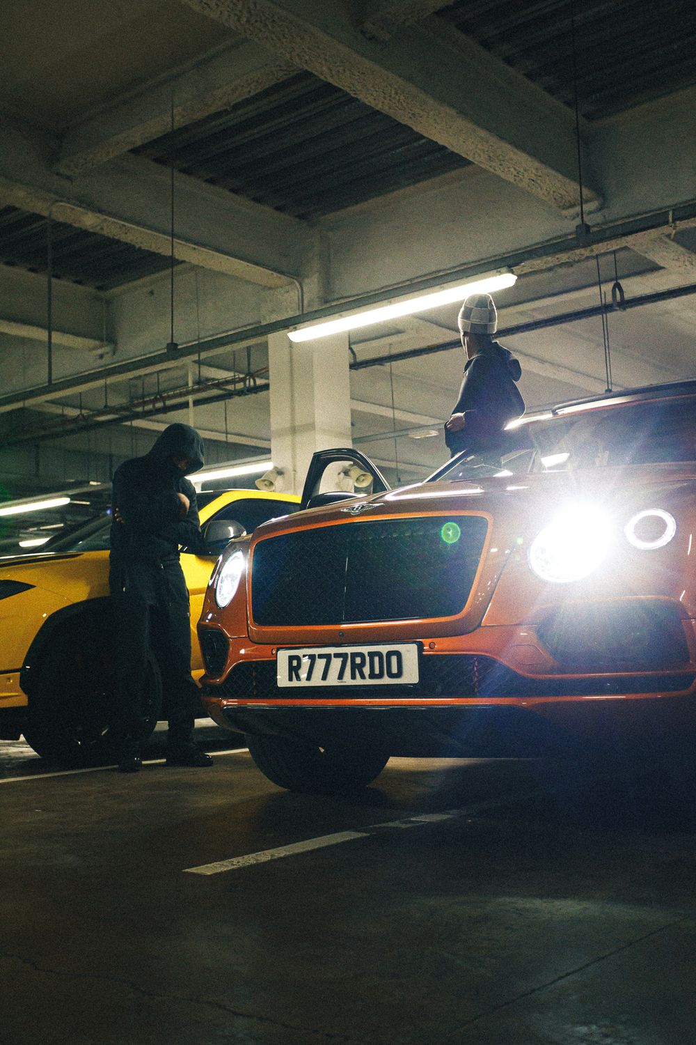 A series of luxury sports cars parked in a dimly lit underground garage with dramatic headlight illumination.