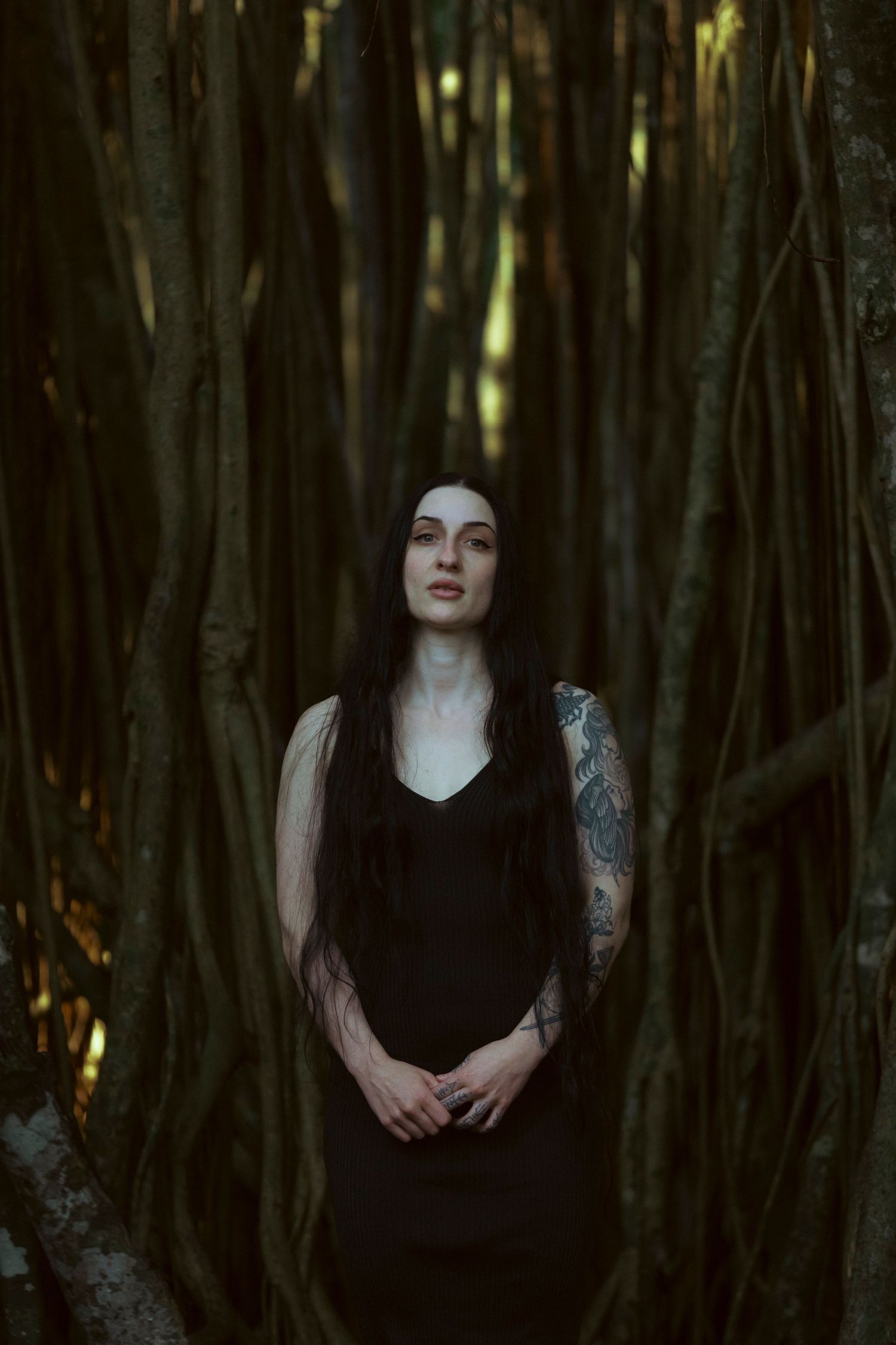 A dark and moody portrait series in a forest setting shows a figure in black against shadowy tree trunks and filtered light.