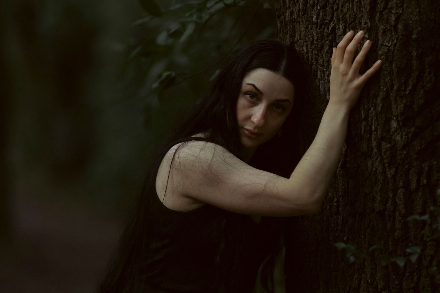 A couple shares an intimate moment in a forest setting with soft natural lighting and lush greenery in the background.