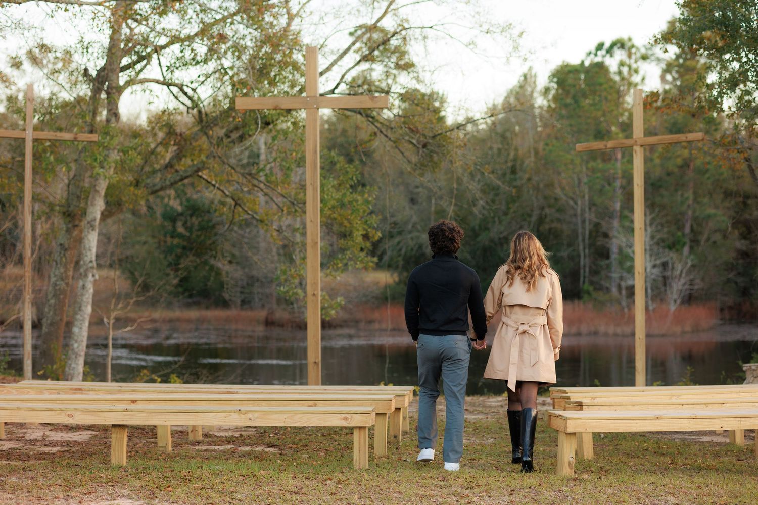 Two people stand at a wooden observation deck overlooking a scenic natural landscape at sunset.