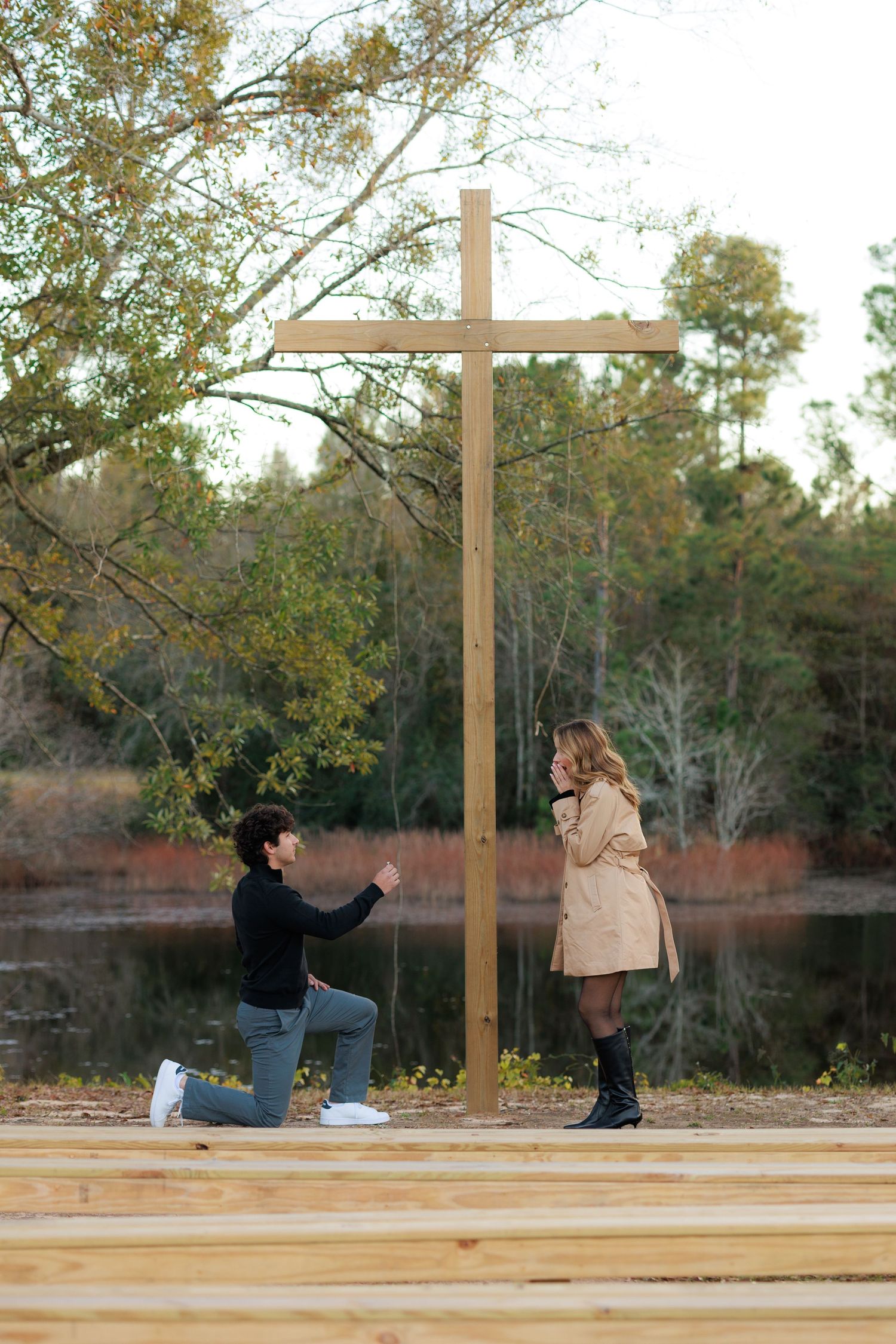 A sequence of photos showing a marriage proposal taking place in front of a wooden cross at sunset by a lake.