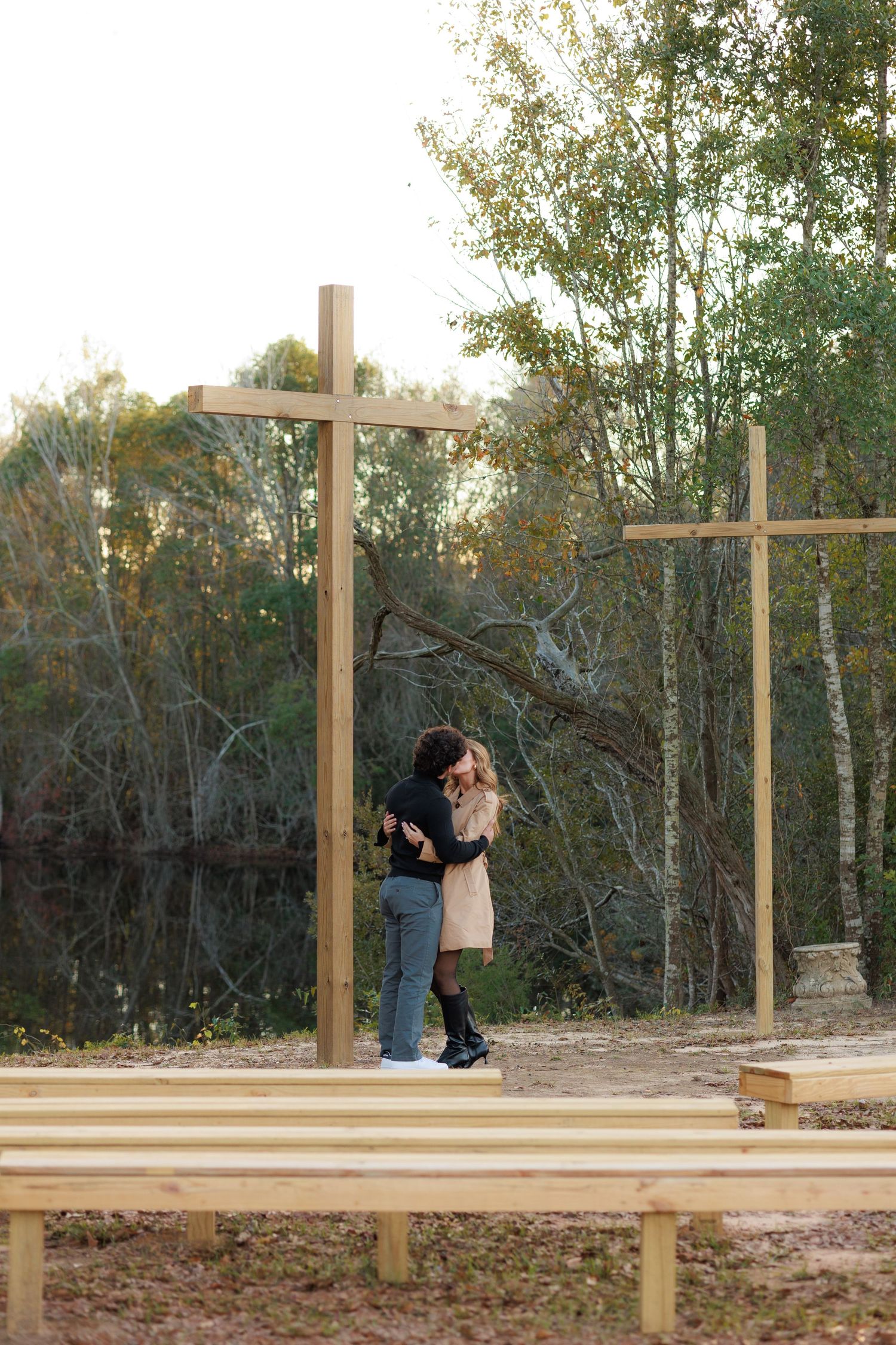 A couple shares an intimate moment on a wooden deck platform with wooden crosses in a natural wooded setting.