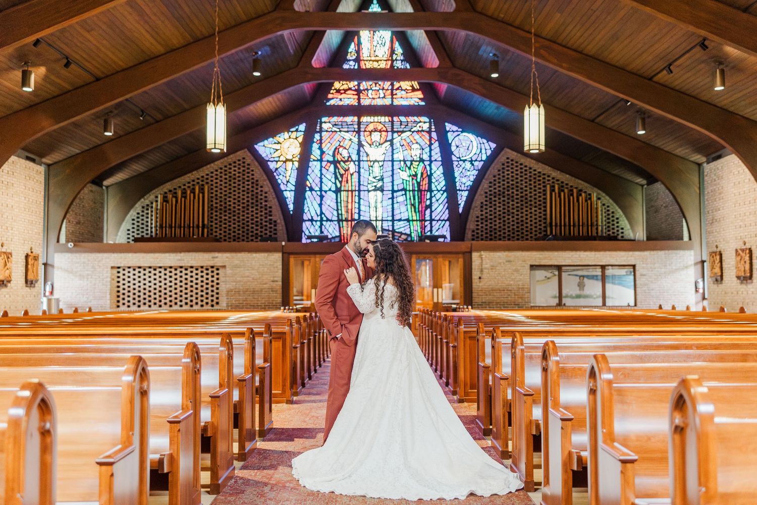 Traditional church interior with wooden beams, stained glass windows and white wedding dress displayed.