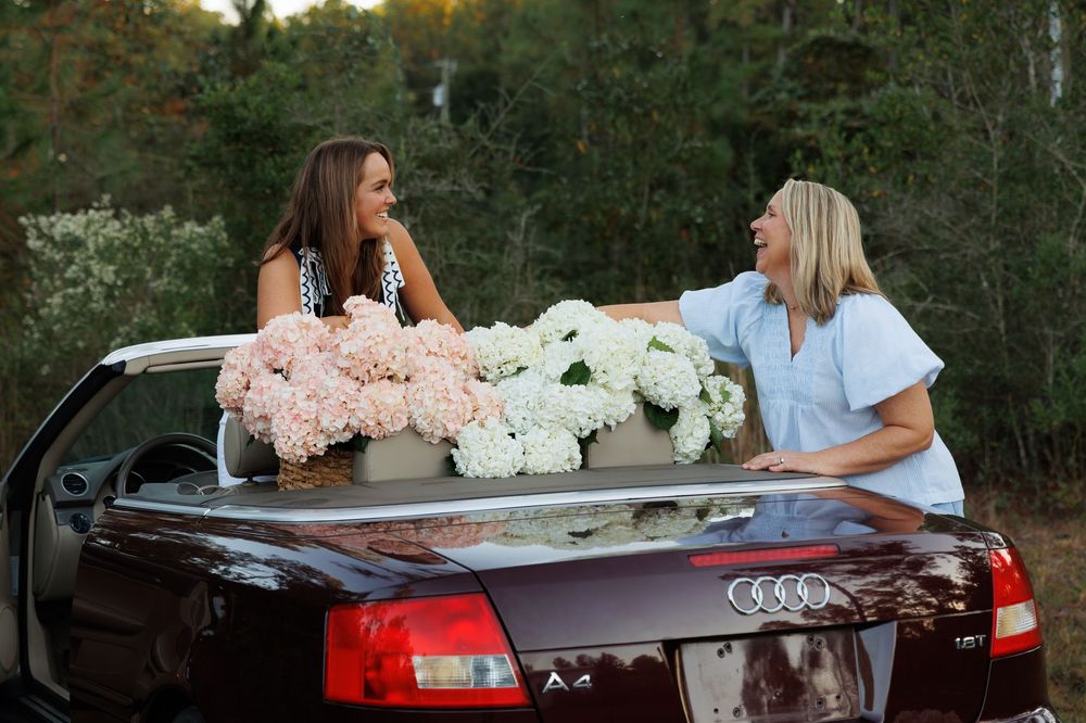 Two people chat while sitting in a black Audi convertible filled with white flowers during a sunset photo session.