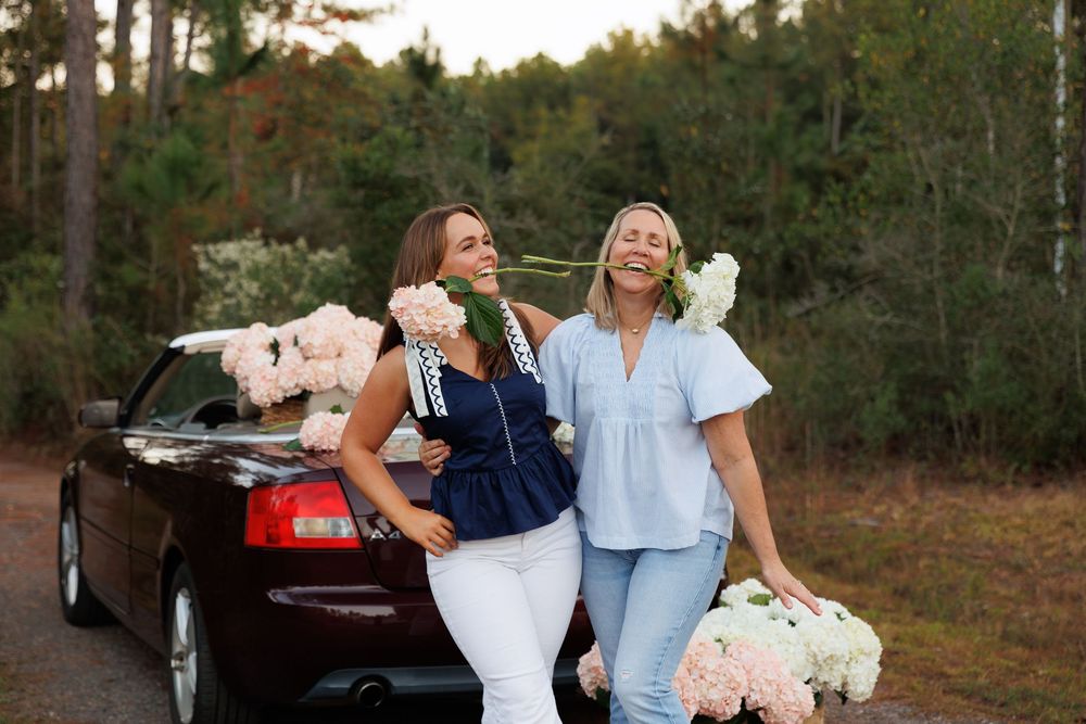 Two people in white outfits share joyful laughter while sitting together outdoors during golden hour.