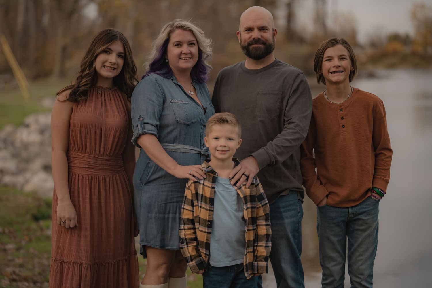 Family of five poses together outdoors in coordinated fall-colored outfits.