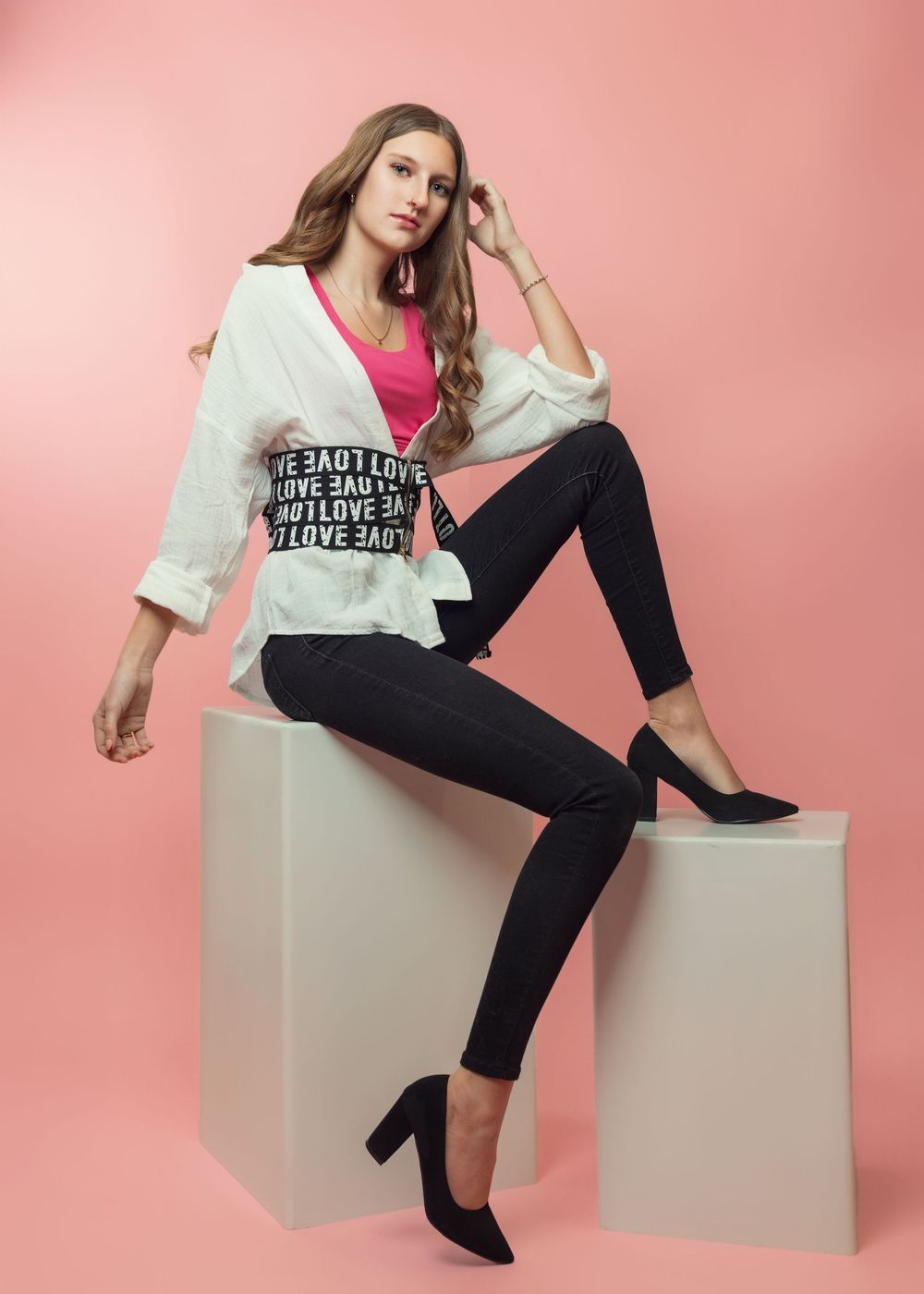 Fashion model in pink and black athleisure outfit poses on white geometric blocks against pink backdrop.