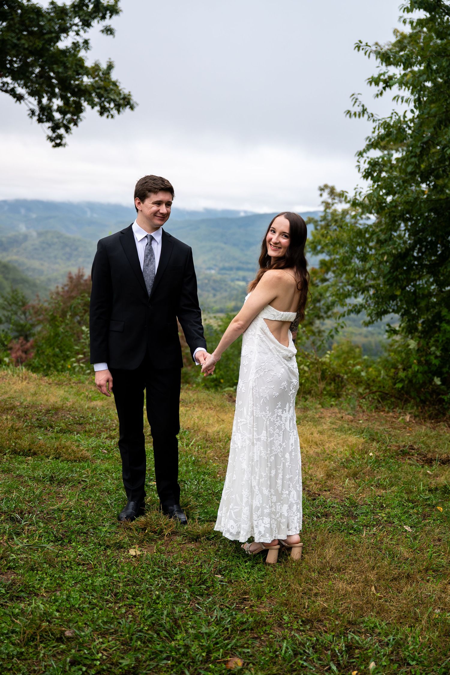 A winter wedding couple embraces on a mountain deck with scenic views and evergreen floral bouquet details.