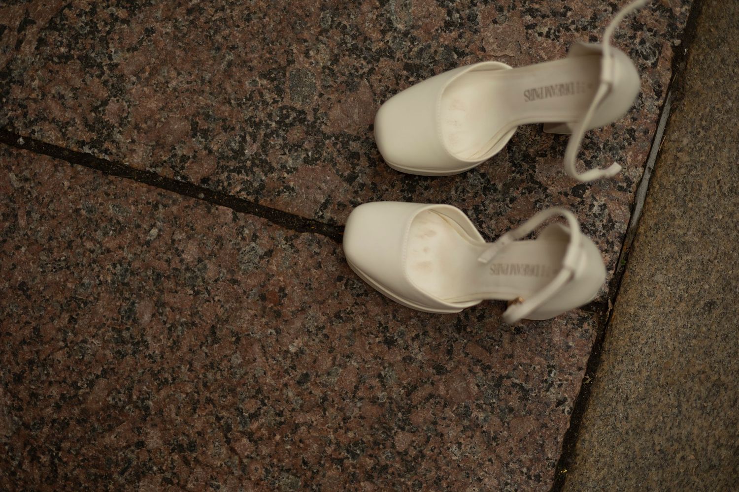A pair of white slingback heels sits abandoned on a granite floor surface.