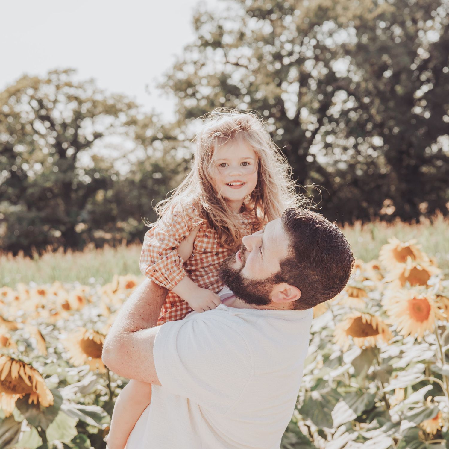 Father lifting his young child in a sunflower field during a warm, natural family photoshoot.