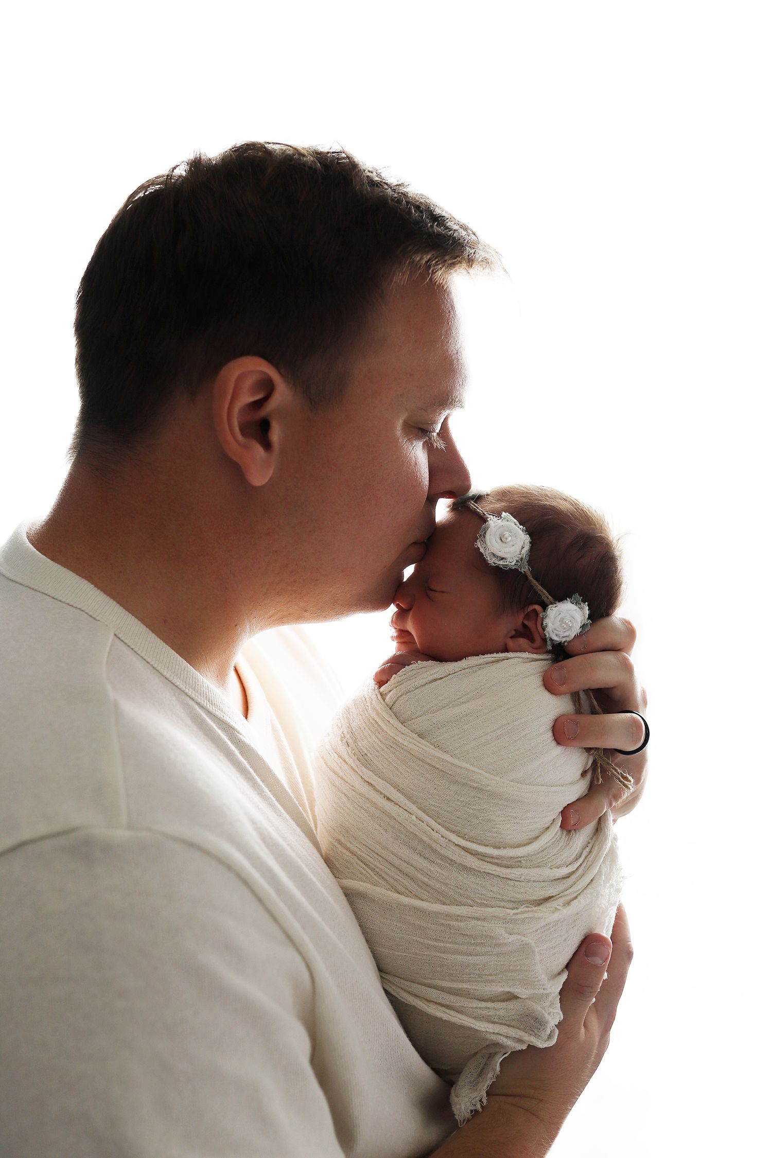 Parents sharing intimate moment with swaddled newborn in soft natural lighting.