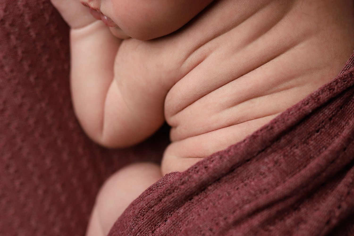 Close-up detail of soft baby skin against burgundy textured fabric.