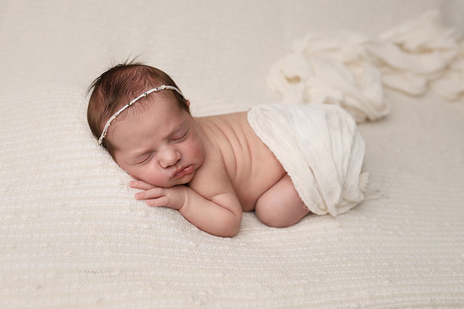 Sleeping newborn in white wrap on textured cream backdrop with delicate headband. Santaquin Utah newborn photography, in-home session