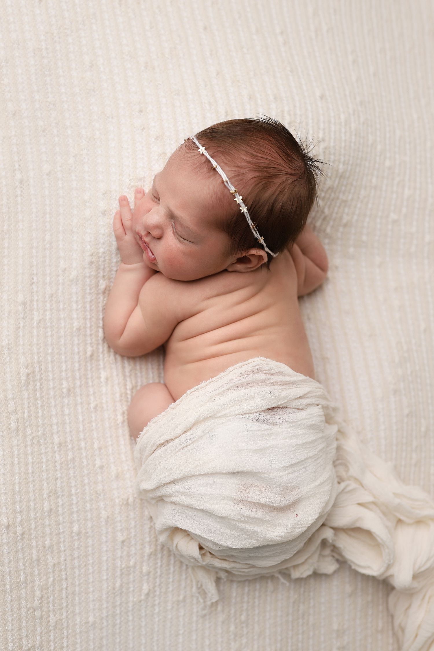A sleeping newborn baby wearing a white wrap lies on a light colored background in a series of peaceful poses.