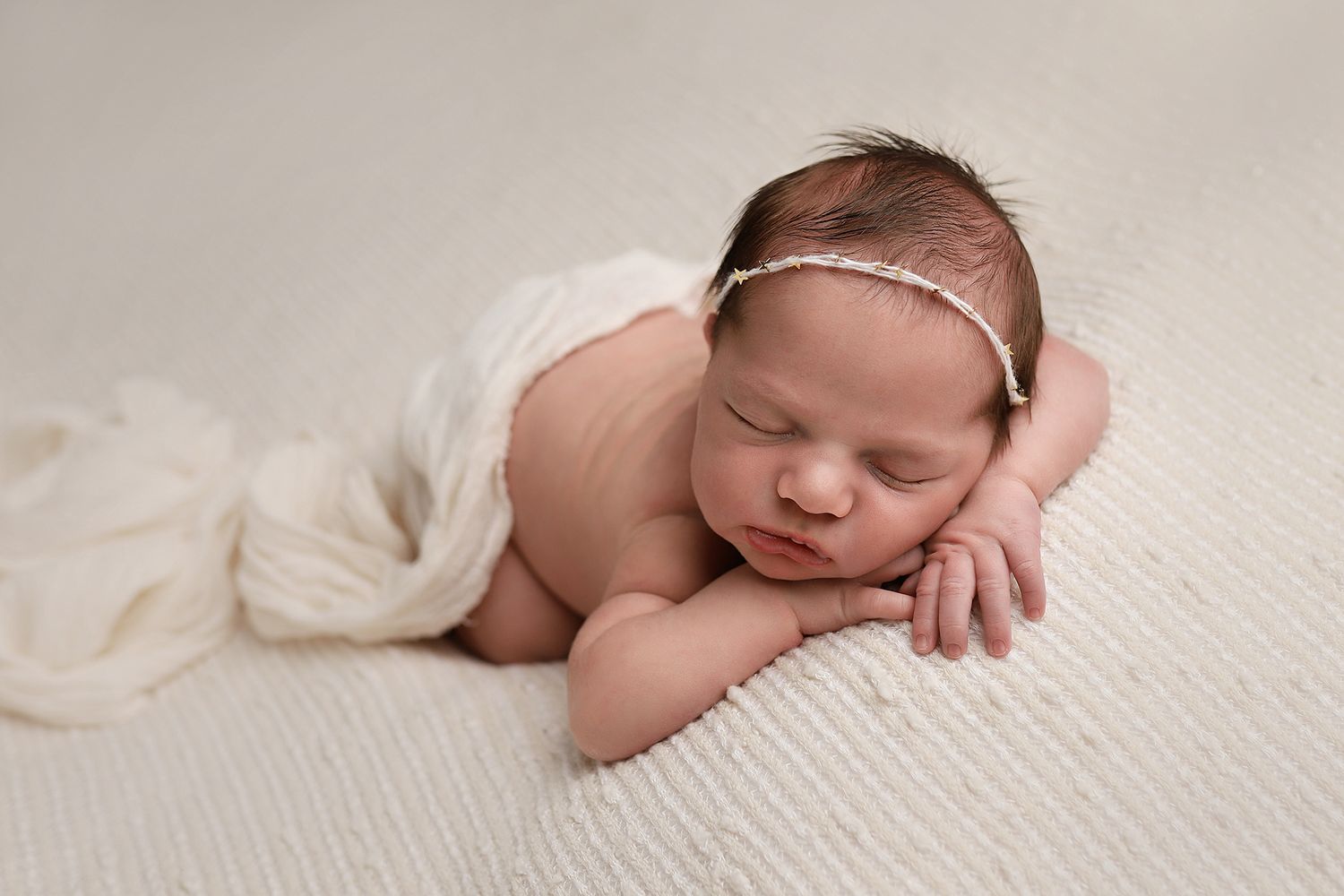 Peaceful newborn resting on cream blanket wearing a dainty headband.