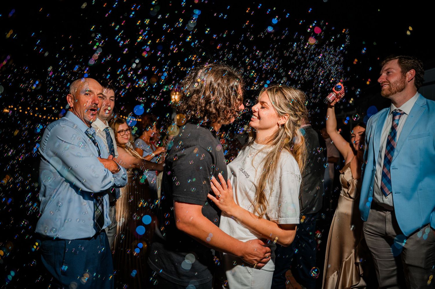 Guests dancing and celebrating at a lively wedding reception with colorful lights and confetti in the air.