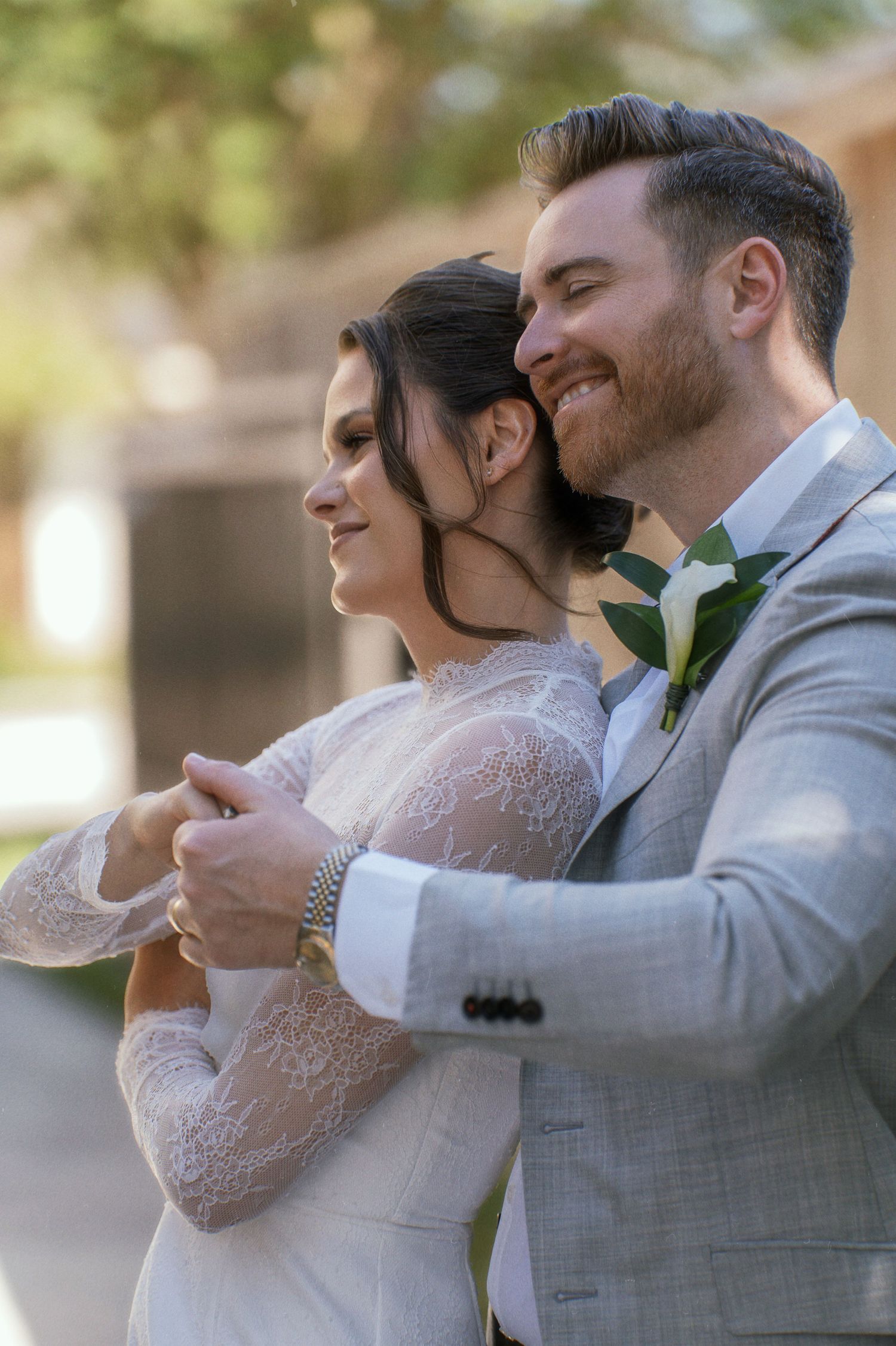 A newlywed couple embraces outdoors in elegant wedding attire.