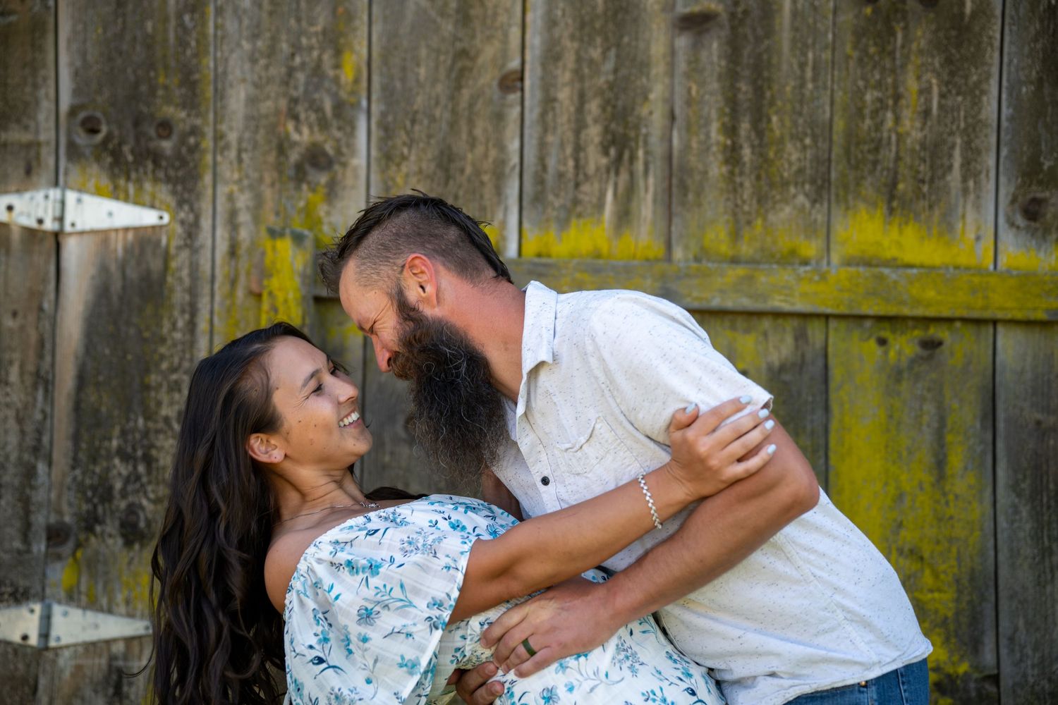 A couple shares a joyful dance moment together against a rustic wooden fence background.