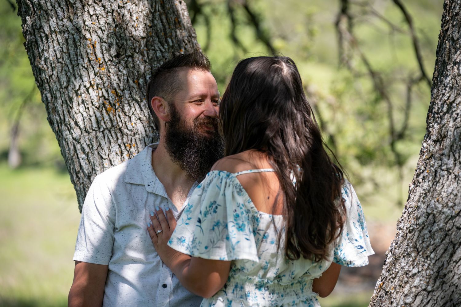 A couple shares a tender moment outdoors among trees in a natural setting.