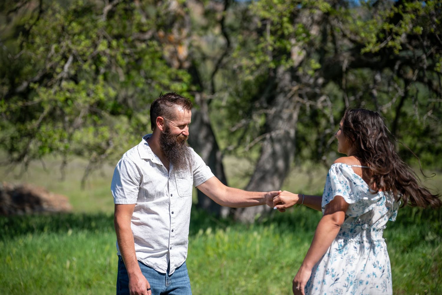 Couple sitting in a grassy meadow surrounded by trees on a sunny day enjoying a romantic picnic together.