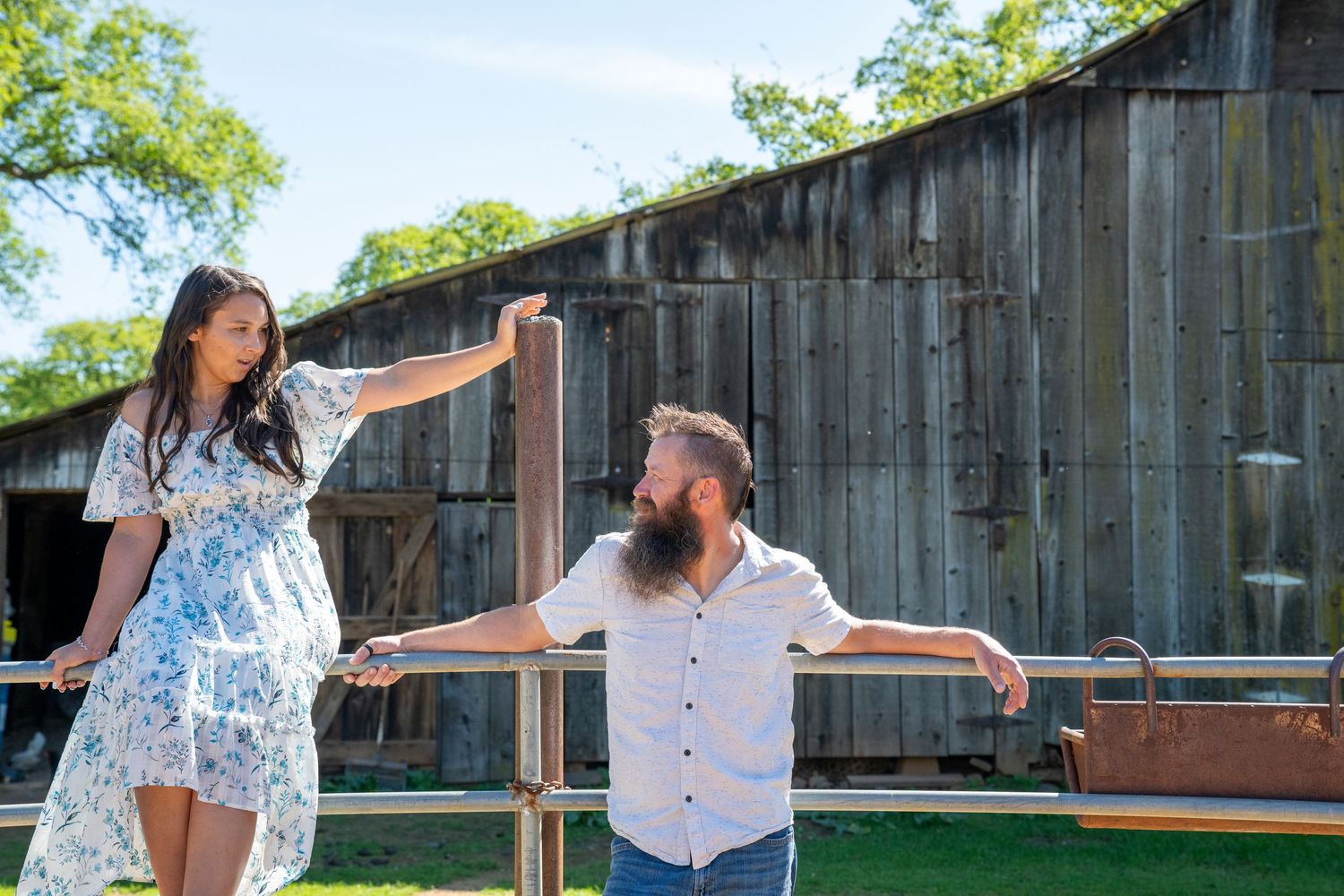 Two people dance together outdoors in front of a rustic wooden barn on a sunny summer day.