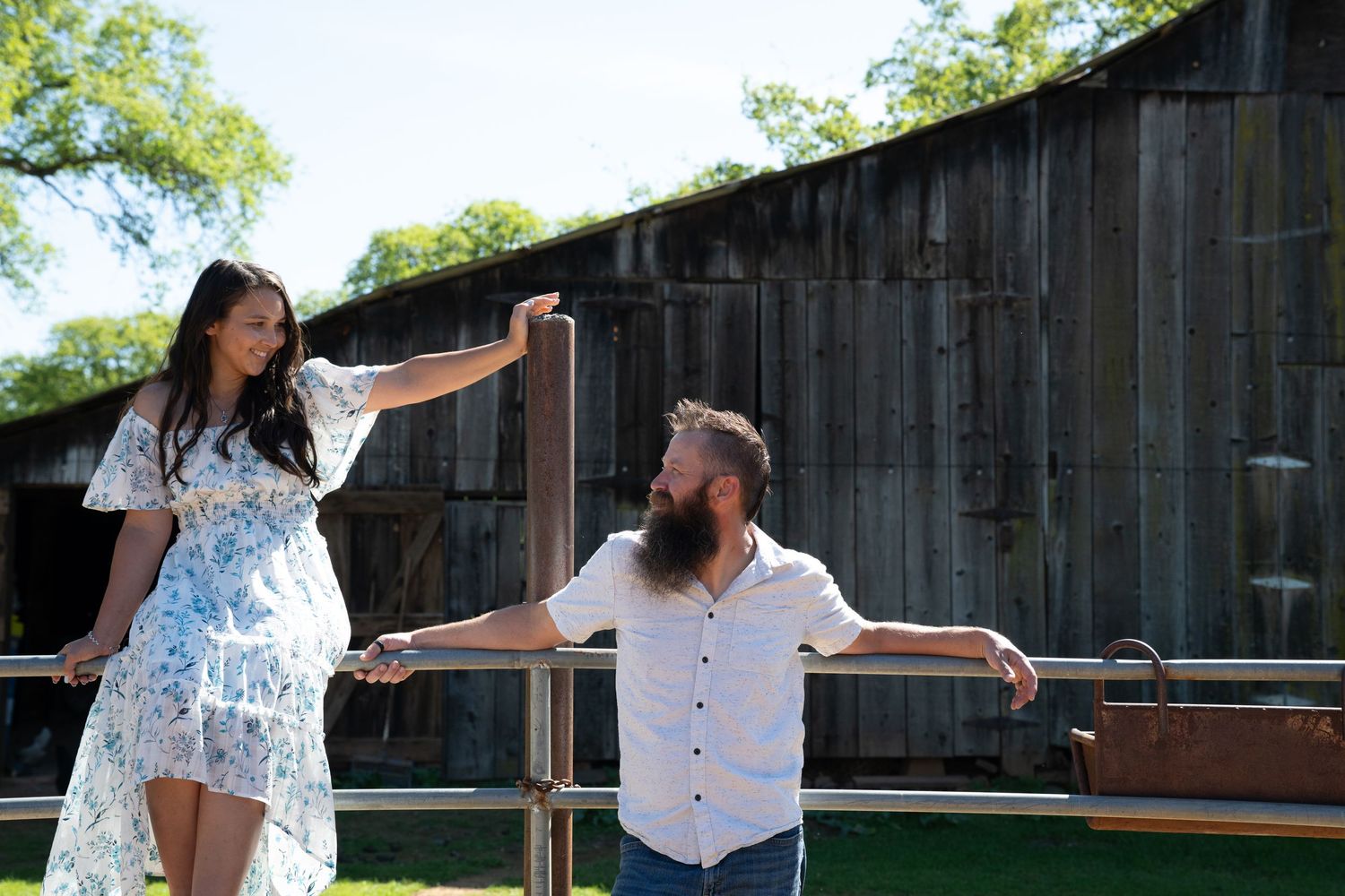 A couple dances together outdoors in front of a rustic wooden barn on a sunny afternoon.