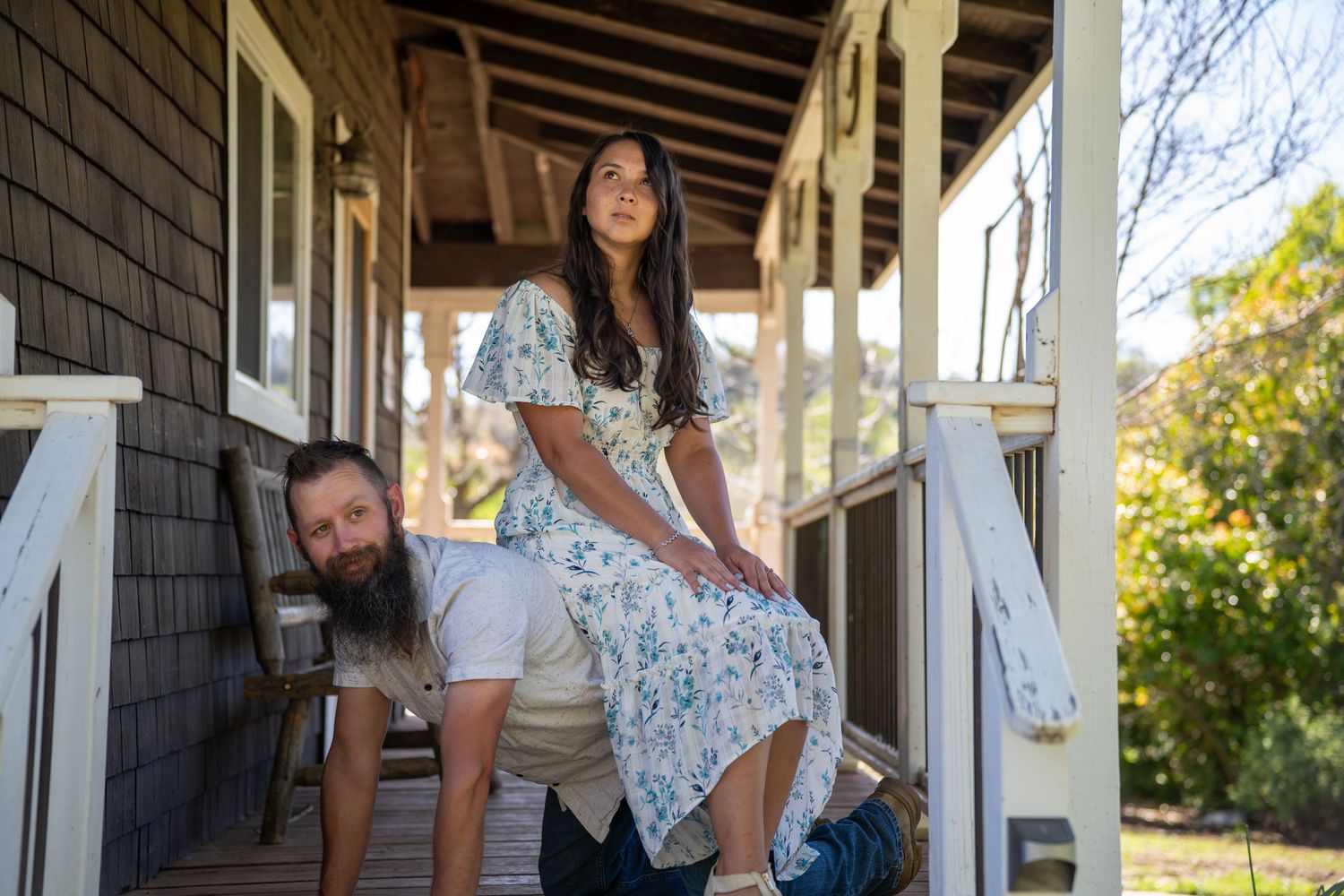 People having fun on a rustic wooden porch of a house with gray shingle siding on a sunny day.