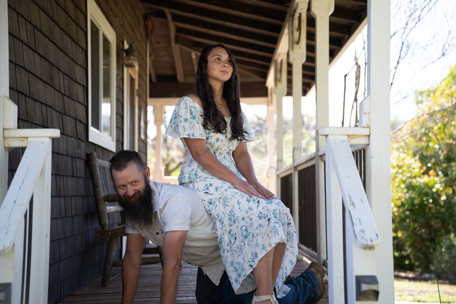 A bride in a lace wedding dress poses under a covered porch in natural lighting.