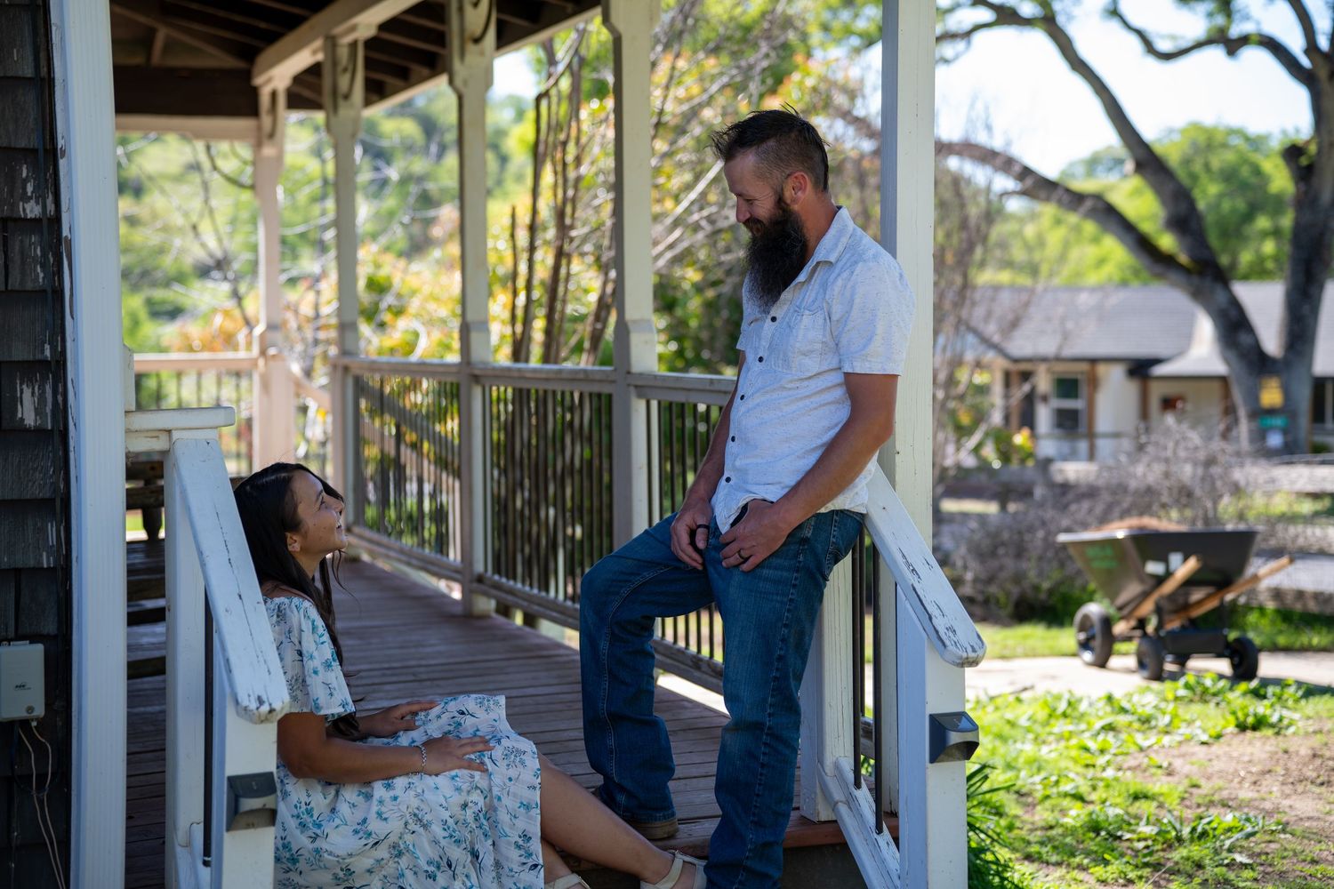 A couple shares a romantic moment on a white porch swing surrounded by lush greenery and natural light.