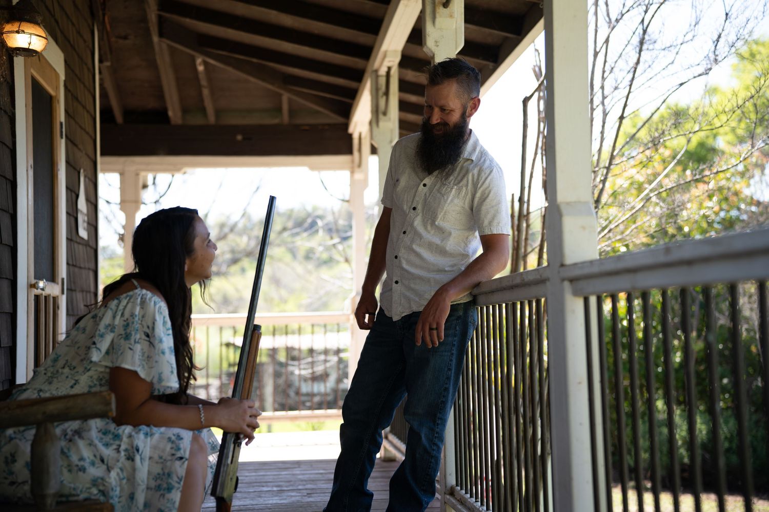 People relaxing on a covered porch with wooden railing and columns on a sunny afternoon.