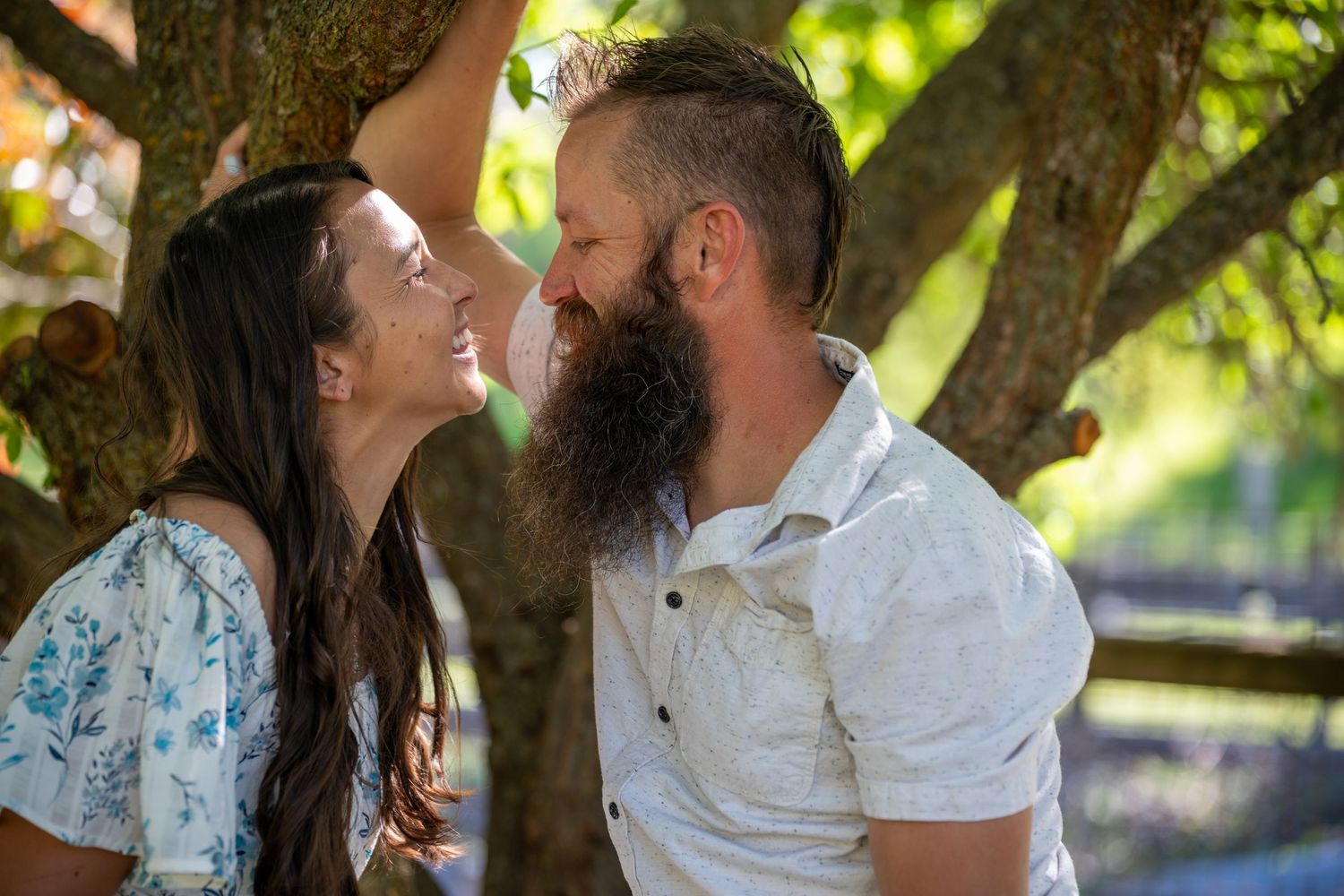 A couple shares romantic moments in a garden setting with dappled sunlight filtering through the trees.