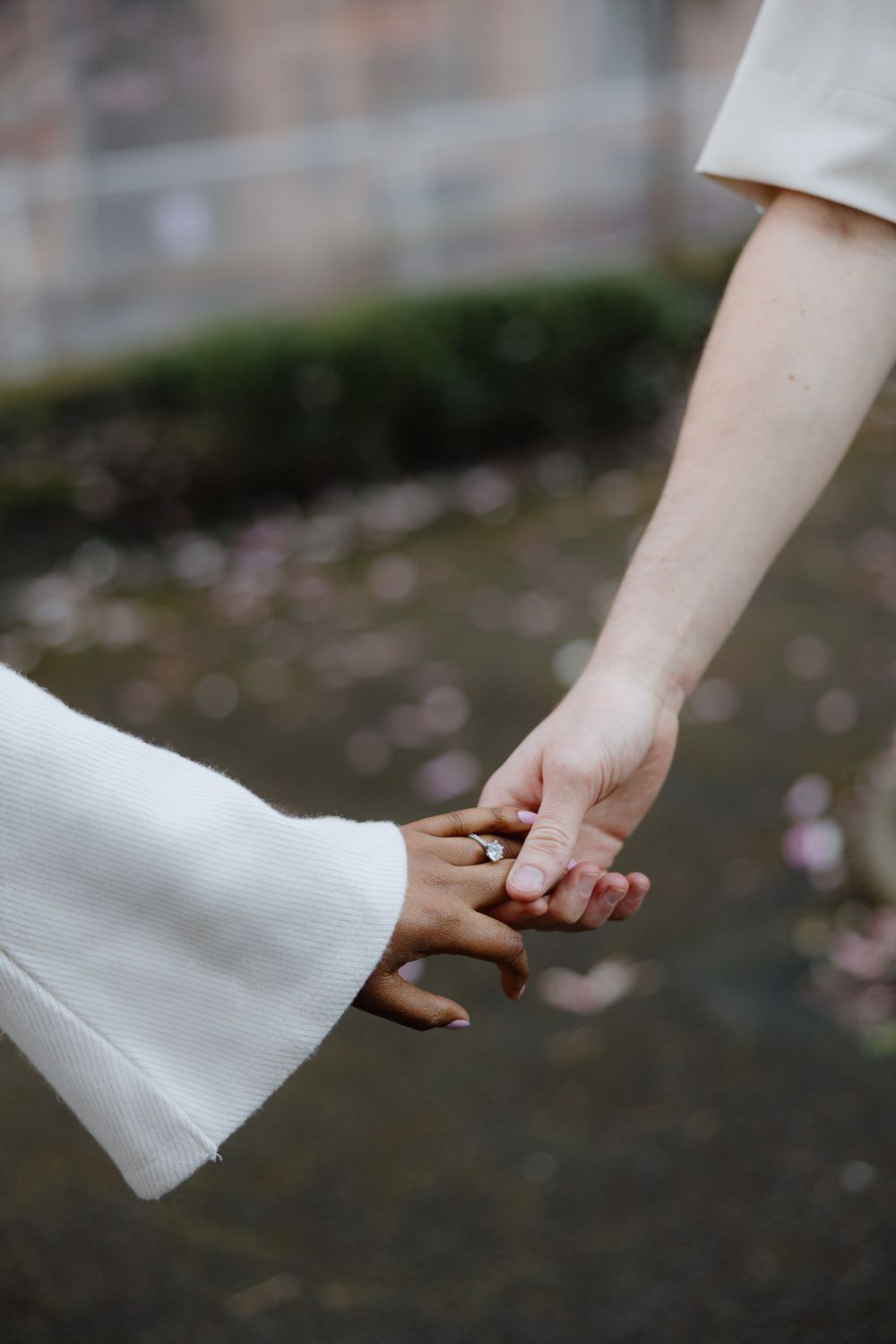 Two hands gently clasped together against a blurred natural background in a romantic gesture.