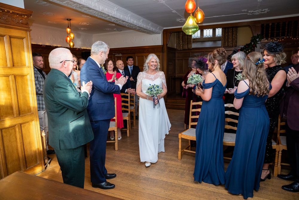 Bride walking down the aisle with bridesmaids in navy dresses at a rustic winter wedding ceremony.