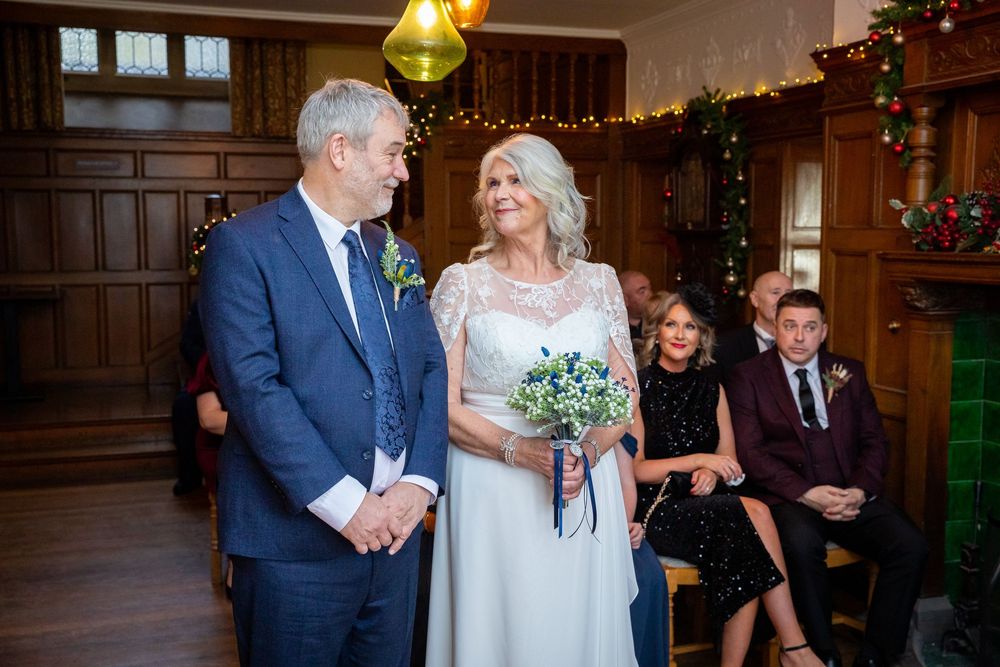 Bride and groom standing together during wedding ceremony in a wood-paneled room with Christmas decor.