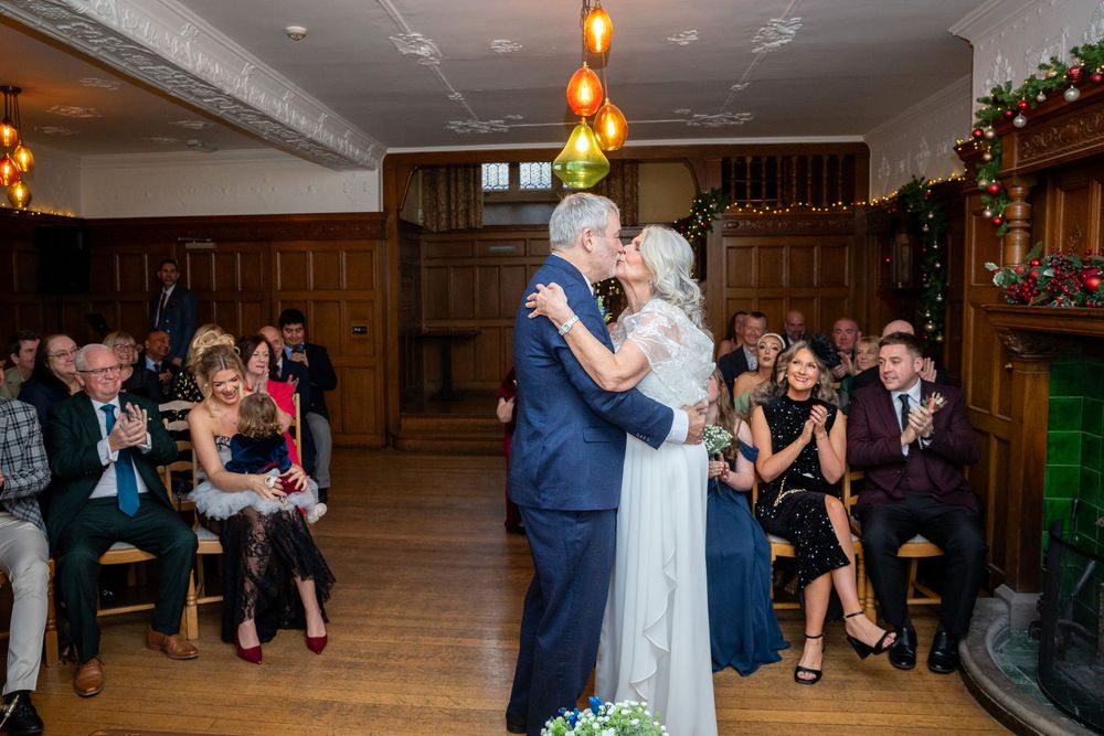 Bride and groom sharing their first kiss surrounded by applauding guests at a winter wedding ceremony.