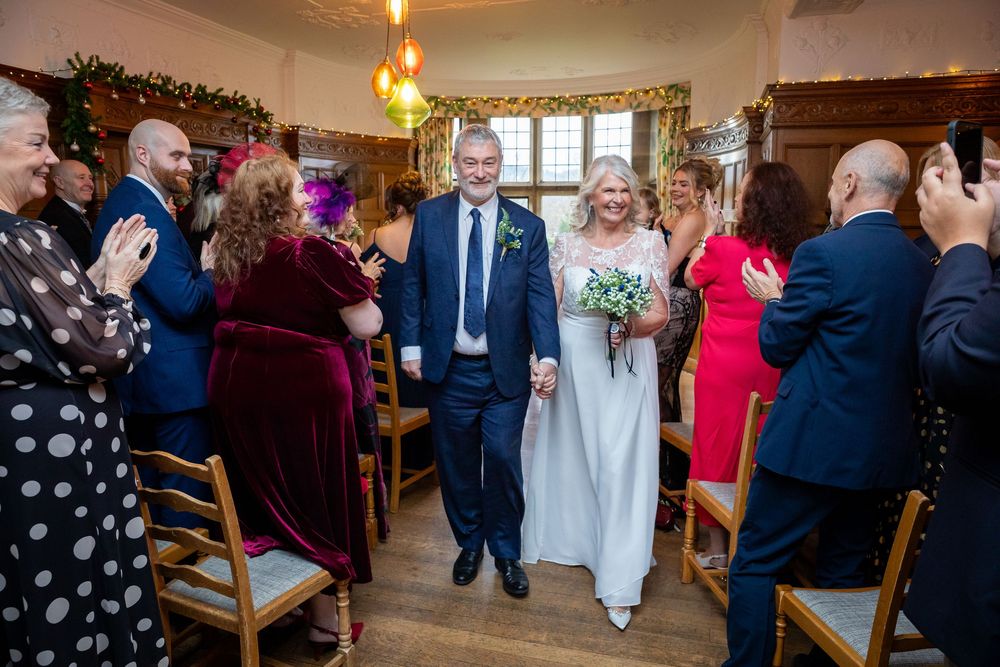 Newlyweds walking hand-in-hand down the aisle as guests applaud at their winter wedding ceremony.