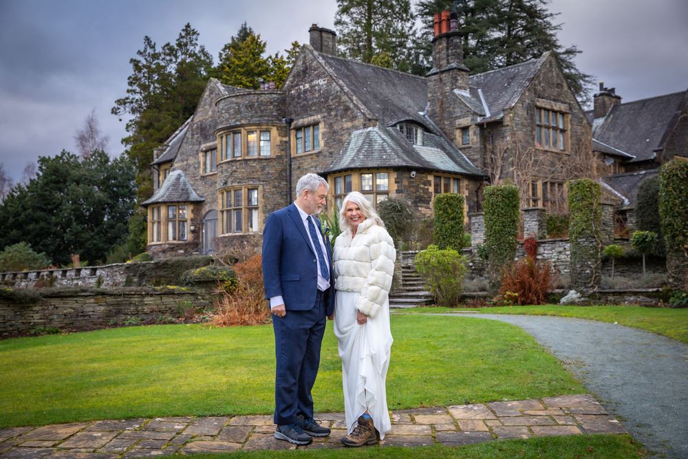 Bride and groom posing together on the grounds of a grand stone manor house on their winter wedding day.