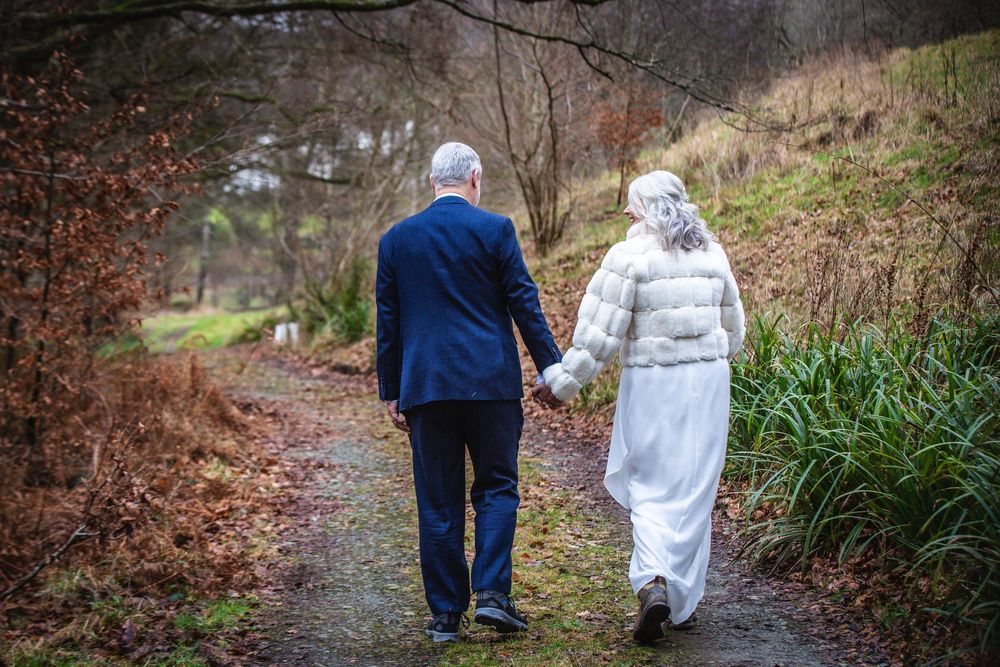 Bride and groom walking hand-in-hand along a woodland path on their winter wedding day.