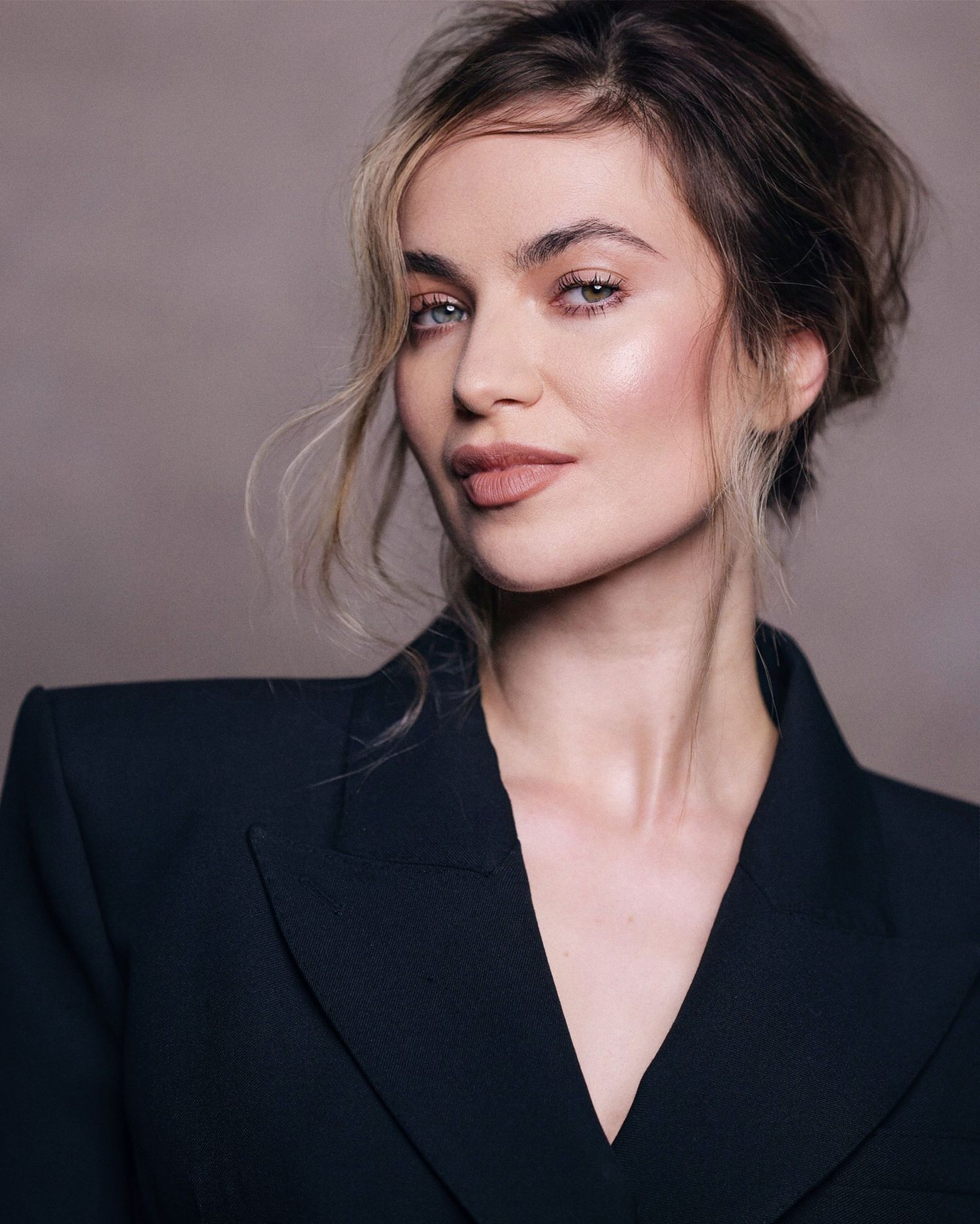 Fashion model wearing an oversized black blazer poses against a gray studio backdrop in a minimalist portrait series.