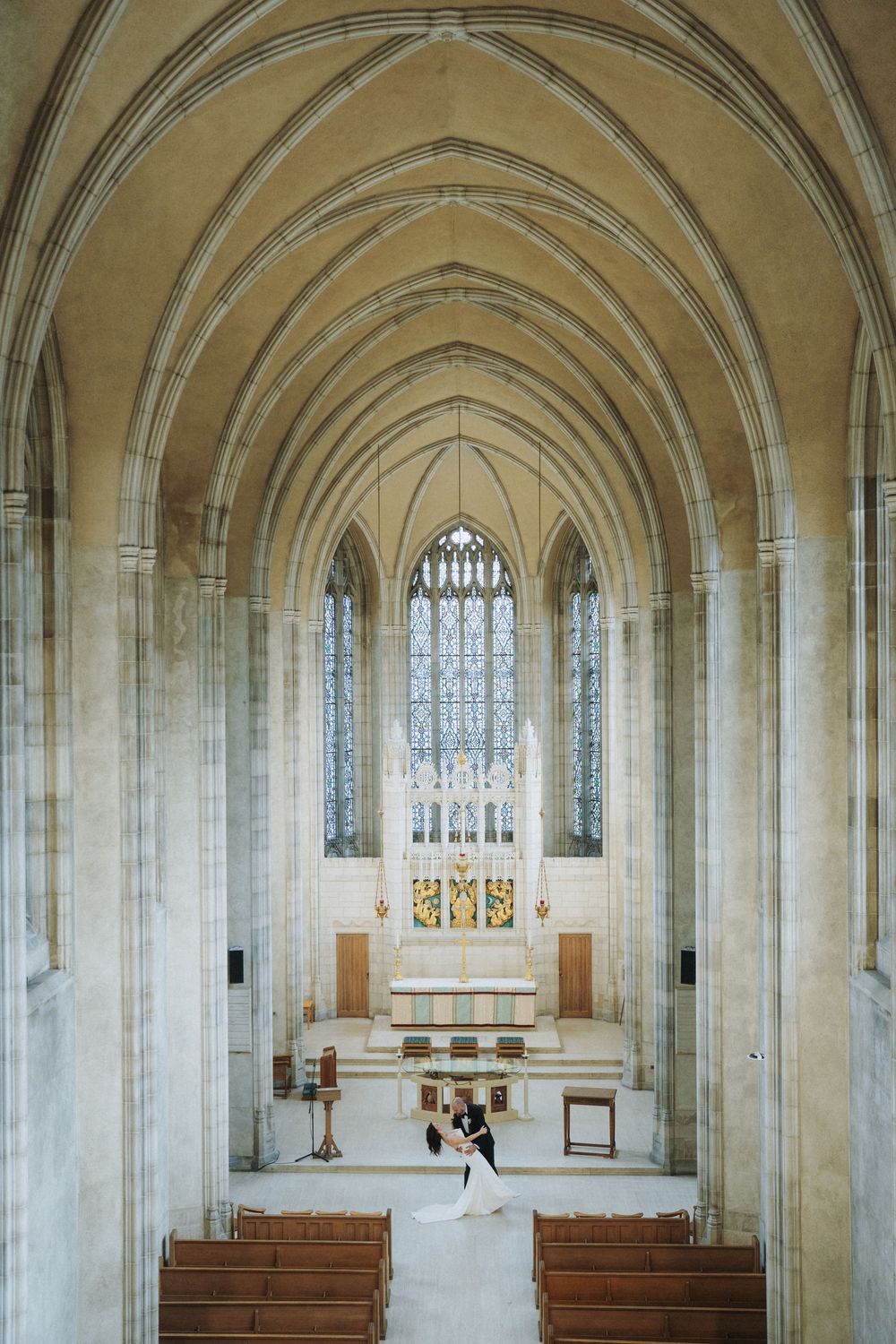 Bride and groom share first dance at the altar of a stunning Gothic cathedral with soaring arched ceilings and stained glass.
