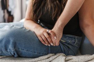 Close up view of hands resting on denim jeans against a textured fabric surface.
