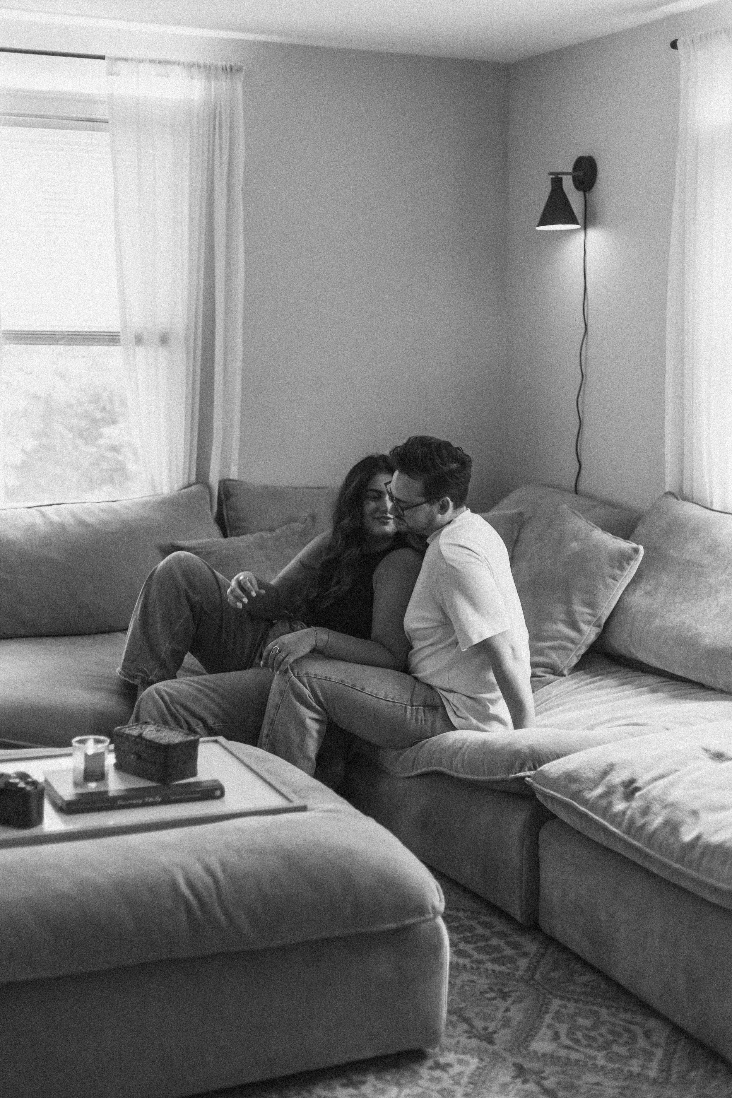 A couple relaxes together on a comfortable gray sectional couch in a sunlit living room.