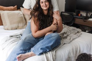 Woman sitting cross-legged on a white bed with casual denim and relaxed pose.