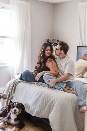Couple relaxing together on bed with their black and white dog in a bright, cozy bedroom.