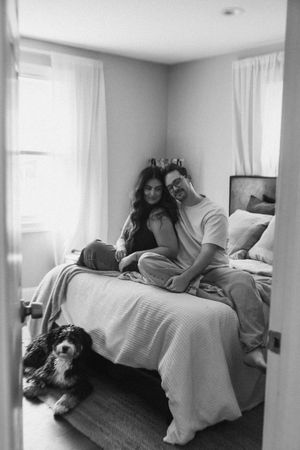 A couple lounges on a white-covered couch with their pet dog in a bright room.